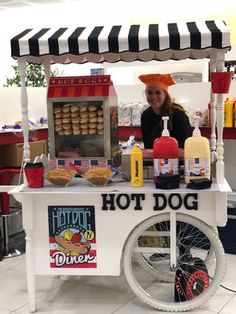 a woman standing behind a hot dog cart with food on the table and in front of it