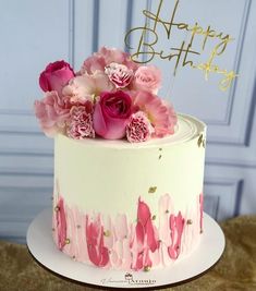 a white cake with pink flowers on top and happy birthday written in gold lettering above it