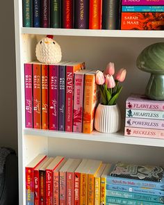 a book shelf filled with lots of books next to a lamp and vase full of tulips