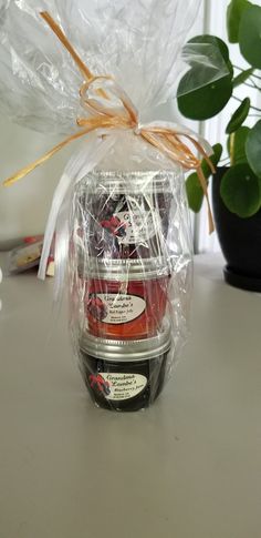 three jars of jam wrapped in plastic and sitting on a table next to a potted plant