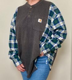 a woman standing in front of a white wall wearing a plaid shirt and blue jeans