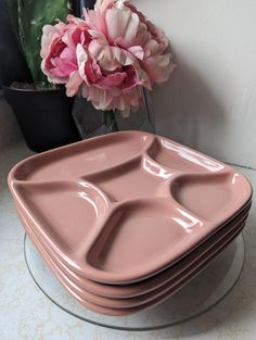 a stack of pink plates sitting on top of a table next to a vase with flowers