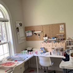 a room with several crafting supplies on the desk and in front of a window