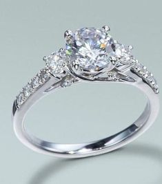 an engagement ring with three stones on the side and one stone in the middle, surrounded by diamonds