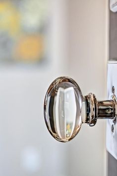 a close up of a glass door handle on a white cabinet with a mirror in the background