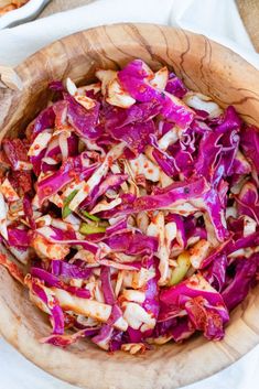 a wooden bowl filled with lots of red cabbage and other food on top of a table