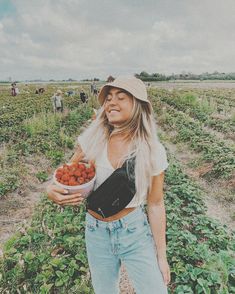 a woman standing in a field holding a bowl of carrots and looking at the camera