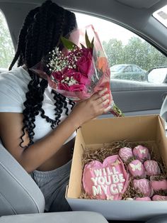 a woman sitting in the back seat of a car holding a bouquet of flowers and cookies