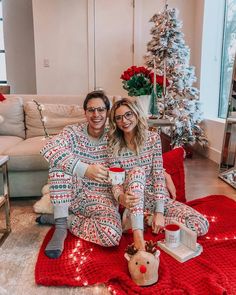 a man and woman sitting on the floor in matching christmas pajamas, holding coffee cups