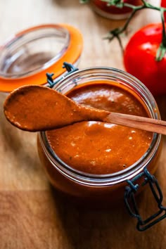 a wooden spoon sitting in a jar filled with sauce next to some tomatoes and peppers