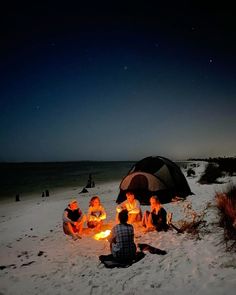 people sitting around a campfire on the beach at night