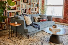 a living room filled with furniture and bookshelves next to a window covered in plants