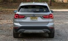 the back end of a silver bmw suv parked in a gravel lot with trees and bushes behind it