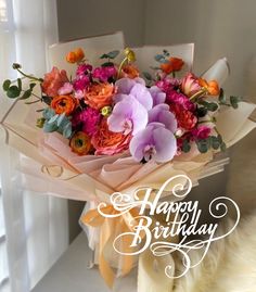 a bouquet of flowers sitting on top of a white table next to a window with the words happy birthday written in it