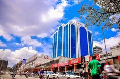 a man walking down the street in front of a tall building with blue and white windows