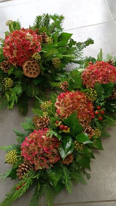 three wreaths with red flowers and green leaves on the floor next to each other