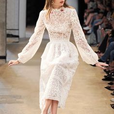 a model walks down the runway in a white dress with long sleeves and high heels