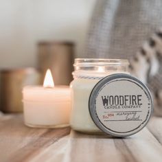 a candle sitting on top of a wooden table next to a glass jar filled with candles