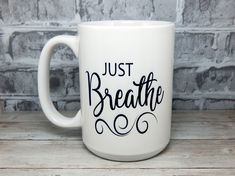 a white coffee mug with the words just breathe on it sitting on a wooden table