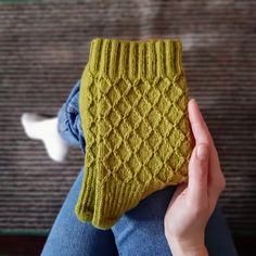 a woman holding up a yellow knitted mitt