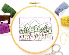 a cross stitch pattern with flowers and mountains in the background, surrounded by yarns