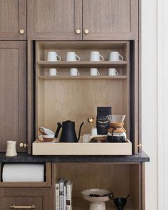 an open cabinet with coffee cups and other items on it in a kitchen area that is well lit by the light