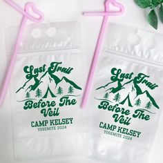 two clear plastic bags with pink straws on top of them next to a green plant