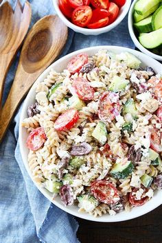 two bowls filled with pasta salad next to wooden spoons and cucumber slices