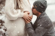 a man and woman standing in the snow holding each other's hands as they kiss