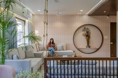 a woman sitting on a couch in a living room next to a large mirror and potted plant