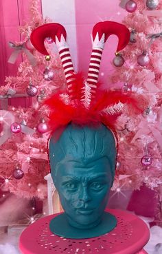 a blue mannequin head with red and white striped stockings on it sitting in front of a pink christmas tree