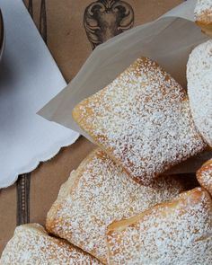 some powdered sugar covered pastries are sitting on a table next to a cup of coffee