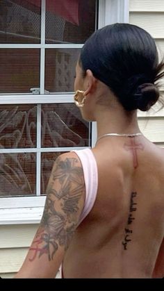 a woman with tattoos on her back standing in front of a window