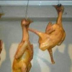 three pieces of chicken hanging from hooks in a kitchen