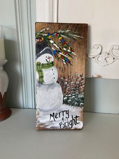 a wooden sign with a snowman painted on it's face and words merry bright