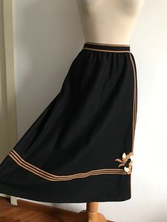 Vintage 70's a-line tailored skirt in good quality medium weight black gaberdine wool with suede / faux suede trimming. Striking geometric line detail going across the bottom of the skirt, the waistband and along the side in a coffee-caramel shade of suede or faux suede fabric. Abstract / floral appliqué design on one side near the bottom.  Back zipper opening secured by hook & eye. Fully lined inside & hidden pockets at each side at hip height. Wide A-line model in a very chic and sophisticated Retro Black A-line Skirt, Black A-line Retro Skirt, Black Retro A-line Skirt, Vintage Knee-length Brown Skirt, Vintage Brown Knee-length Skirt, Retro Black Long Skirt, Vintage Black Lined Skirt, Retro Brown Skirt, Retro Brown Mini Skirt