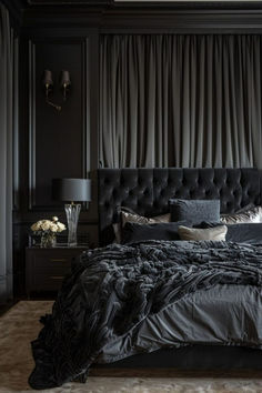 a bed with black sheets and pillows in a dark room next to two lamps on either side of the bed