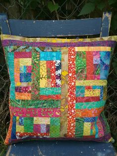 a colorful patchwork pillow sitting on top of a blue chair next to a fence