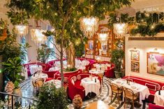 the interior of a fancy restaurant with red booths and white tablecloths, potted plants and chandeliers