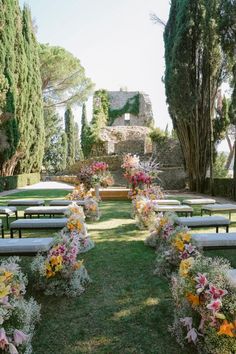 an outdoor ceremony set up with white benches and flower arrangements on the grass in front of trees