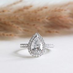 a pear shaped diamond engagement ring with two side stones on the band and a feather in the background