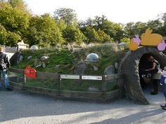 people are standing in front of a fake rock tunnel with grass growing on the top