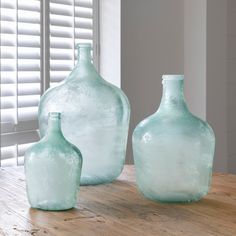 three glass vases sitting on top of a wooden table next to a white window