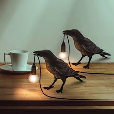 two birds on a table with lights and a coffee cup in front of the lamp