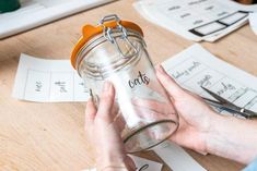 a person holding a glass jar with scissors on top of it next to some papers