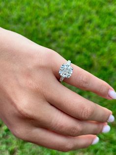 a woman's hand with a diamond ring on top of her finger and grass in the background