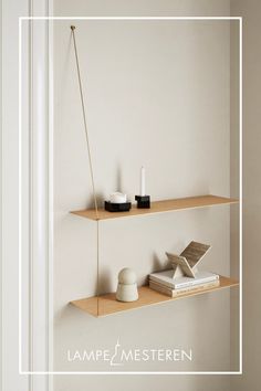 two wooden shelves with books, candles and other items on them against a white wall