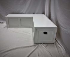 two white drawers sitting side by side on a sheet covered bed with the bottom drawer open