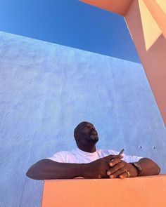 a man leaning against a wall with his cell phone in one hand and looking up at the sky