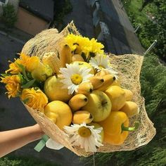 a person holding a bouquet of fruit and flowers in their hand, with the view of a street behind them